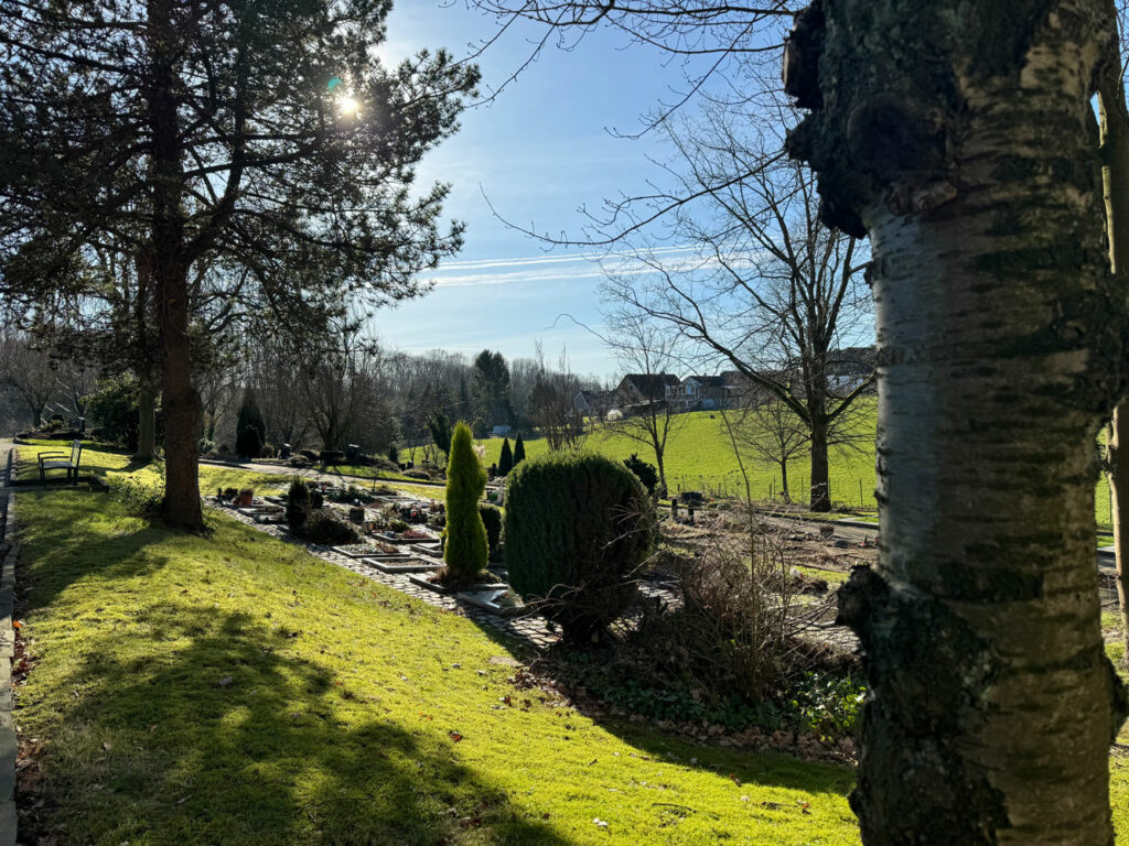 Friedhof in Burscheid mit grünflächen, Bäumen und bepflanzter Grabanlage